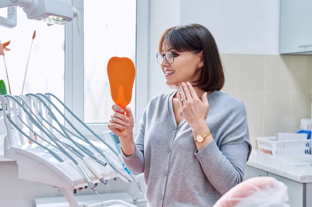 Happy dental patient viewing her new smile in a mirror after cosmetic treatment in Orlando