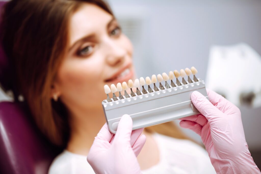 Dentist holding tooth shade guide to compare whitening and veneer options with a patient